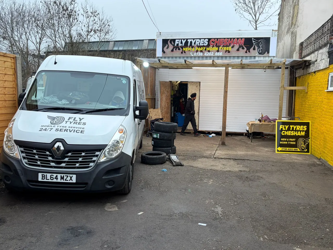 The Fly Tyres van parked outside the unit with the shutter open and tyres stacked in the yard.